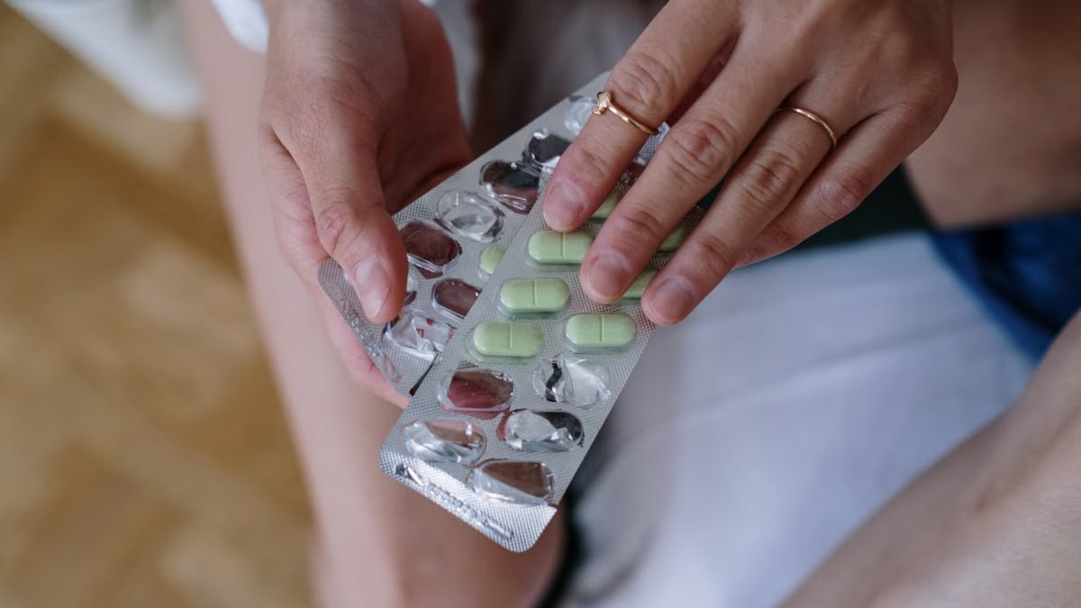 Person holding a blister pack of green tablets, focusing on healthcare and treatment.