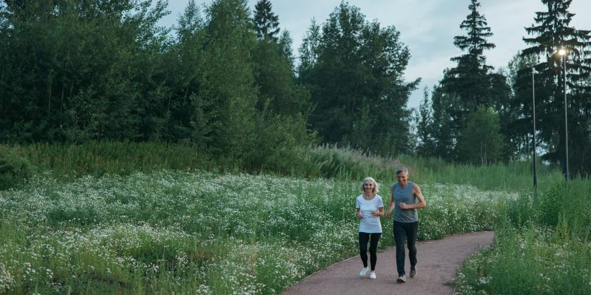 Senior couple jogging on a scenic park path surrounded by greenery.