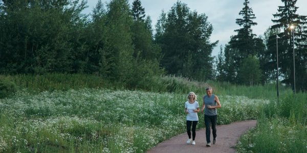 Senior couple jogging on a scenic park path surrounded by greenery.